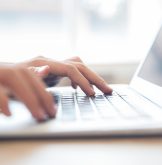 Close-up of male hands typing on laptop keyboard indoors. Businessman working in office or student browsing information